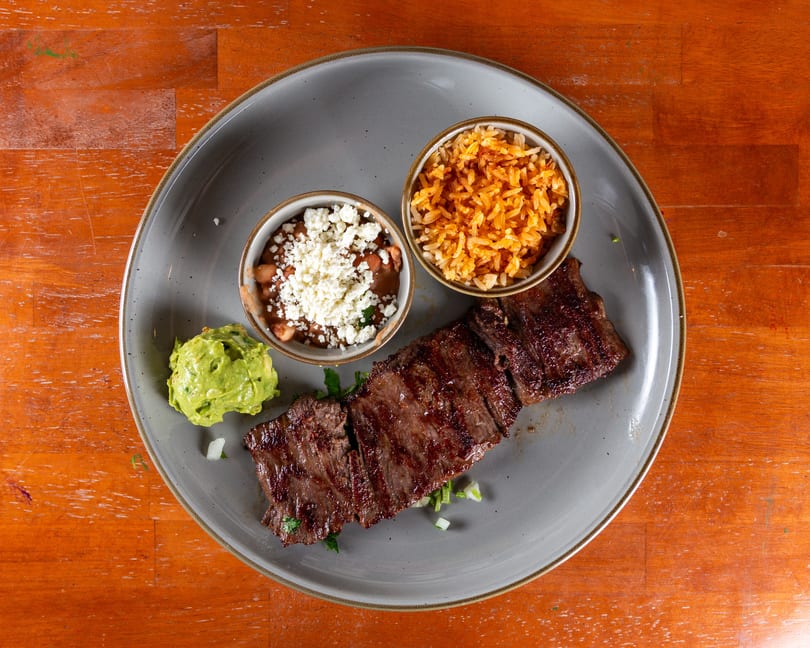 Grilled steak with rice, beans topped with cheese, and guacamole on a gray plate.