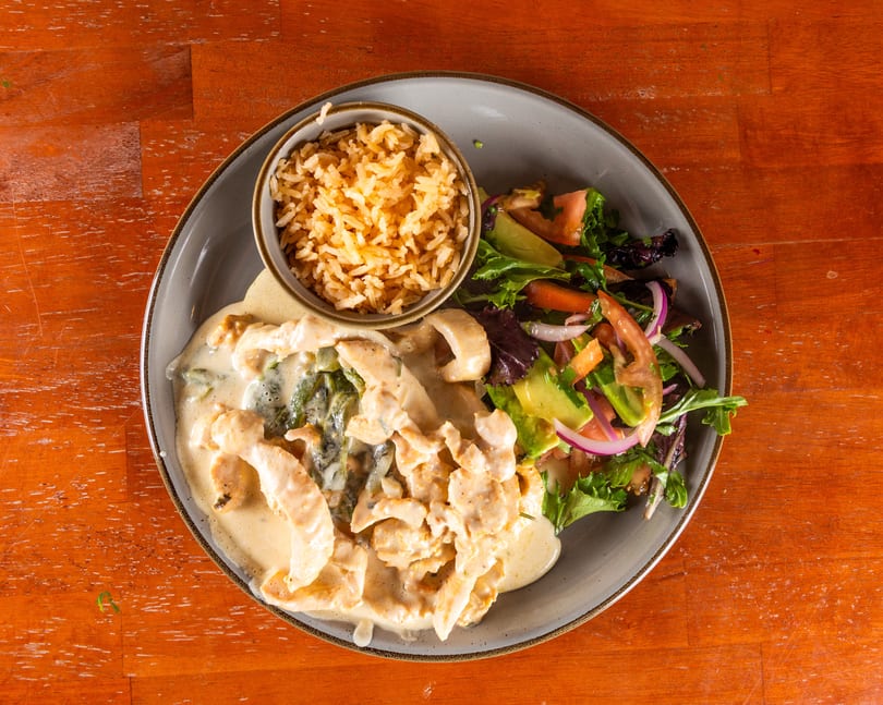 Creamy chicken and poblano peppers with rice and a fresh salad on a wooden table.